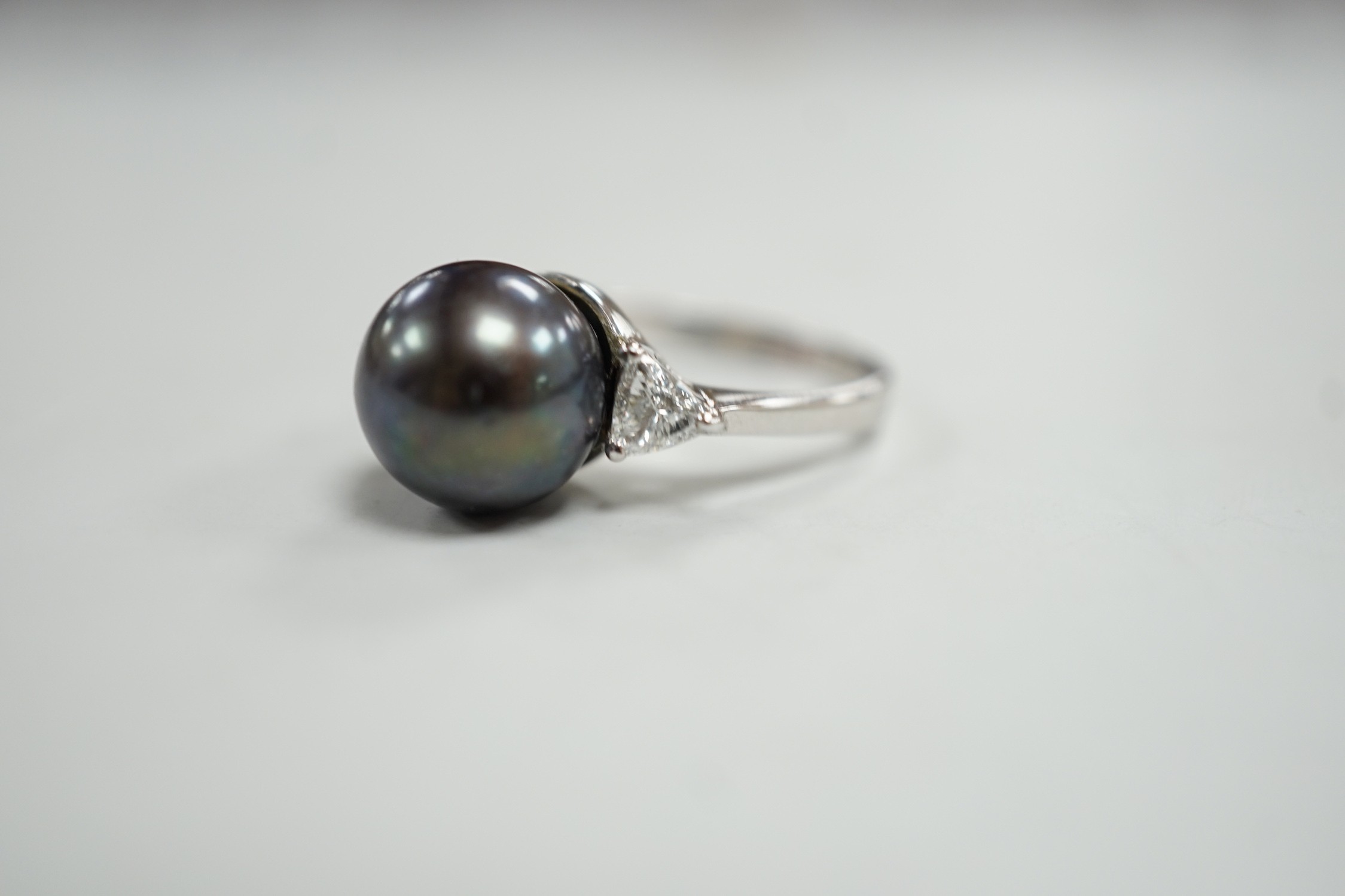 A modern 750 white metal, single stone Tahitian pearl and two stone trillion cut diamond set ring, size O, gross weight 5.6 grams.